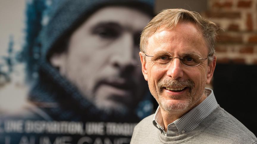 A man with glasses and a tie smiles.